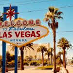 Welcome to Fabulous Las Vegas sign with palm trees and Mandalay Bay hotel in the background under a clear blue sky.